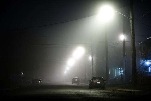 Foggy road at night with cars parked at the side